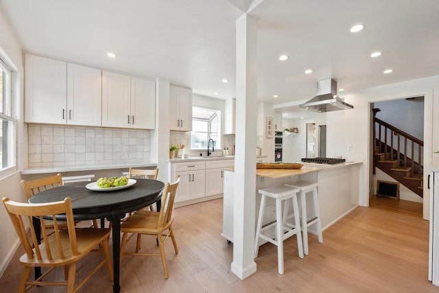 kitchen featuring tasteful backsplash, sink, white cabinets, island exhaust hood, and light wood-type flooring