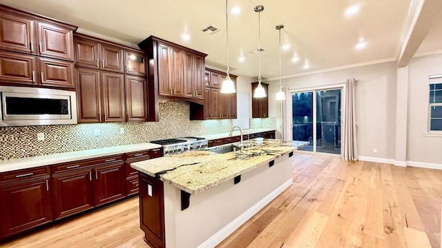 kitchen with sink, range, hanging light fixtures, stainless steel microwave, and light stone countertops