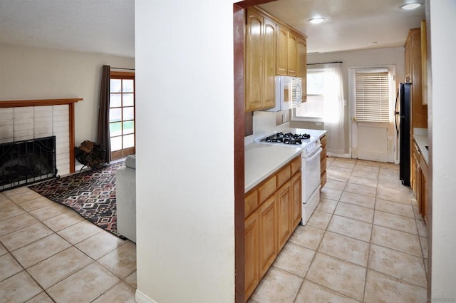 kitchen with white appliances, light tile patterned floors, a fireplace, and light brown cabinets