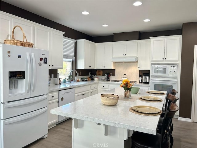 kitchen featuring white cabinets, a kitchen island, white appliances, and a kitchen bar