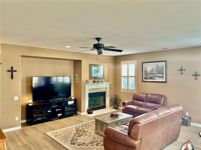 living room with light wood-type flooring, ceiling fan, and a tiled fireplace