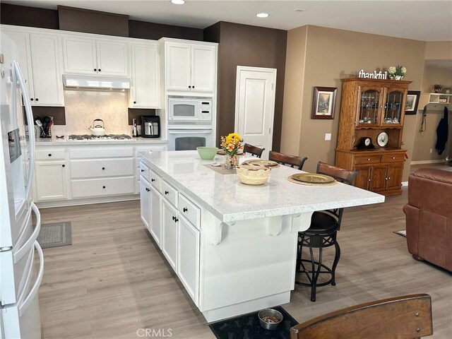 kitchen with white cabinets, a kitchen island, white appliances, and decorative backsplash