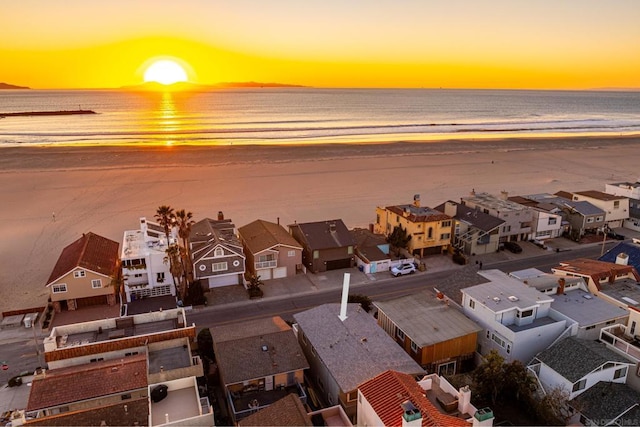 aerial view at dusk featuring a water view and a beach view