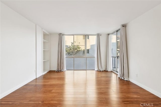 unfurnished room featuring built in features, hardwood / wood-style floors, and a wall of windows