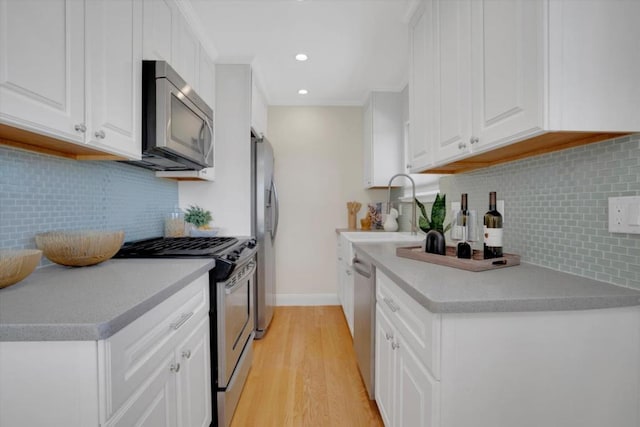 kitchen with sink, white cabinetry, light wood-type flooring, appliances with stainless steel finishes, and backsplash