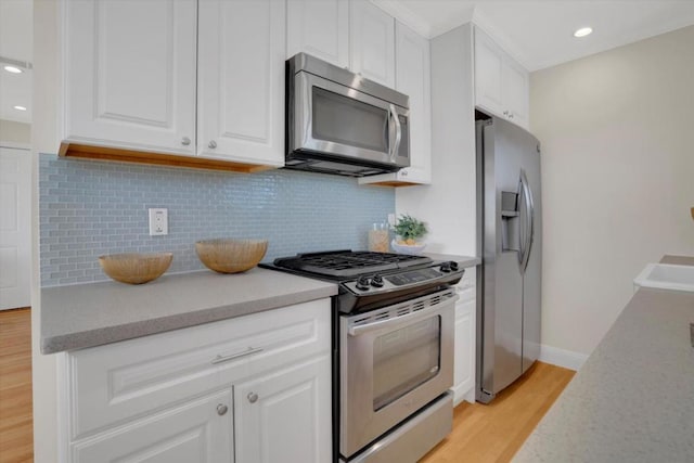 kitchen featuring white cabinetry, appliances with stainless steel finishes, light wood-type flooring, and backsplash