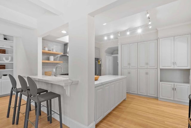 kitchen with kitchen peninsula, light hardwood / wood-style flooring, white cabinetry, refrigerator, and a breakfast bar