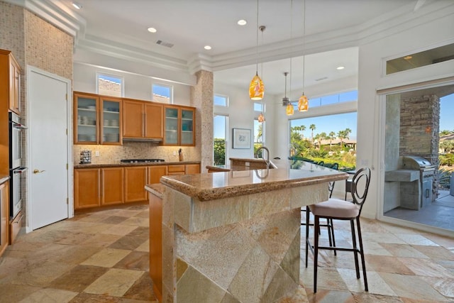 kitchen featuring decorative backsplash, hanging light fixtures, a breakfast bar, a center island with sink, and crown molding