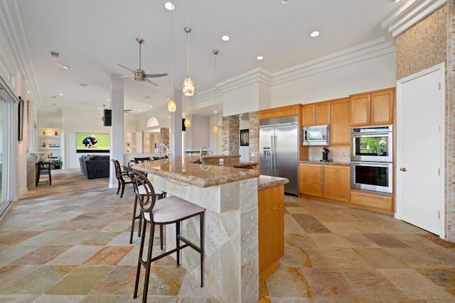 kitchen featuring hanging light fixtures, sink, backsplash, light stone counters, and built in appliances