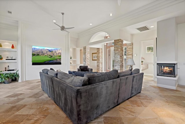 living room featuring ornate columns, a multi sided fireplace, built in features, ornamental molding, and ceiling fan