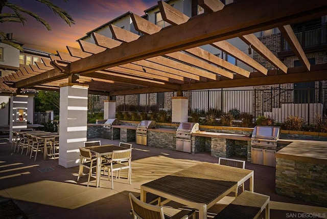 patio terrace at dusk featuring an outdoor kitchen, grilling area, and a pergola