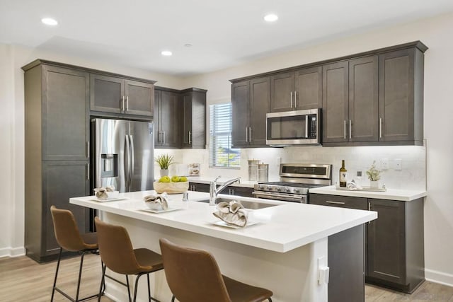 kitchen with a kitchen breakfast bar, dark brown cabinets, appliances with stainless steel finishes, a kitchen island with sink, and light hardwood / wood-style floors