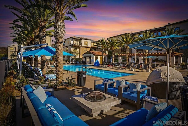 pool at dusk featuring a patio area and an outdoor living space with a fire pit