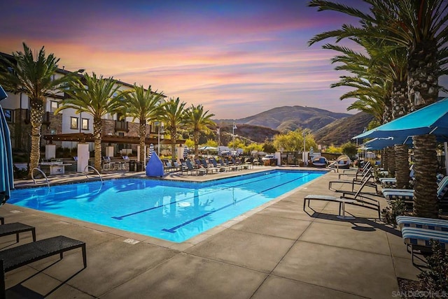 pool at dusk featuring a mountain view and a patio