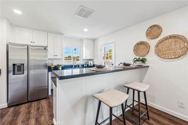 kitchen with white cabinetry, stainless steel fridge, kitchen peninsula, and a kitchen bar