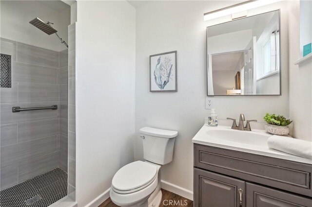 bathroom featuring vanity, wood-type flooring, toilet, and tiled shower