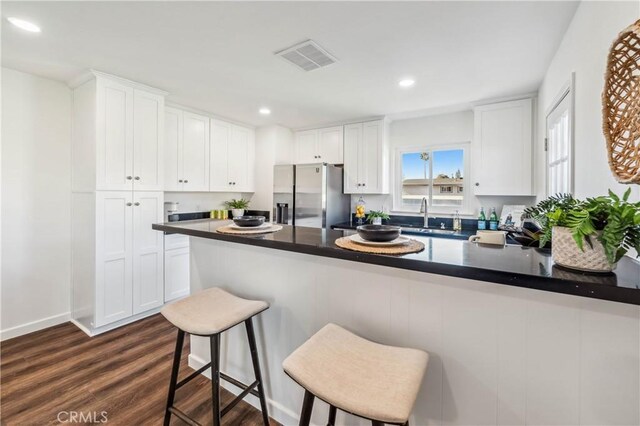 kitchen featuring white cabinetry, stainless steel refrigerator with ice dispenser, sink, and a kitchen bar