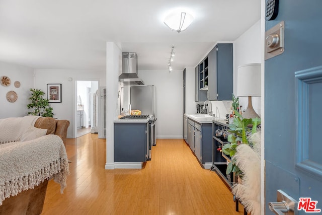 kitchen featuring sink, range hood, blue cabinetry, and light hardwood / wood-style floors