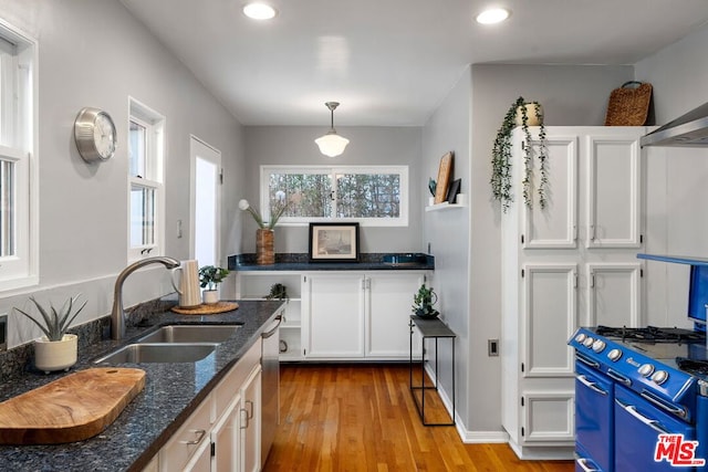 kitchen featuring sink, white cabinetry, decorative light fixtures, dark stone countertops, and light hardwood / wood-style floors