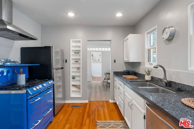 kitchen with white cabinets, sink, gas stove, and wall chimney exhaust hood