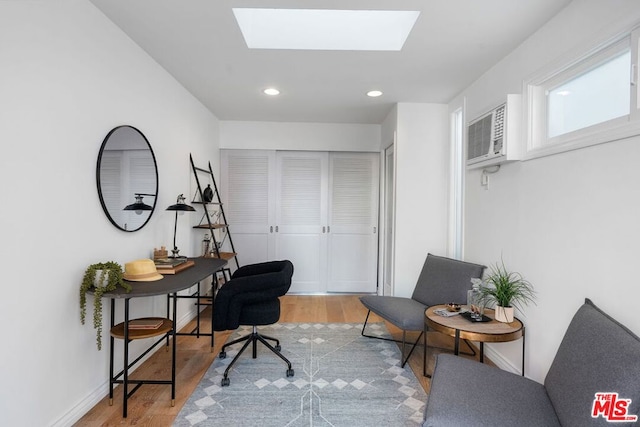 office space with a skylight, a wall mounted air conditioner, and light hardwood / wood-style flooring