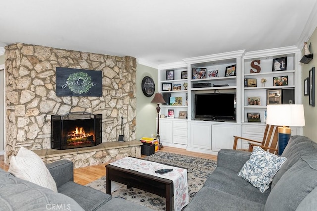 living room with hardwood / wood-style flooring, a stone fireplace, and crown molding