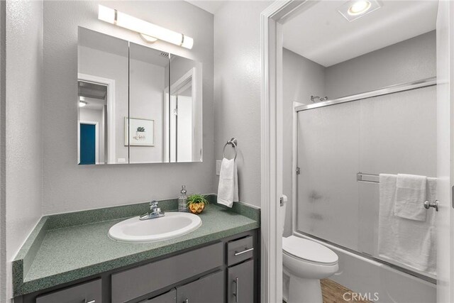 full bathroom featuring wood-type flooring, bath / shower combo with glass door, toilet, and vanity