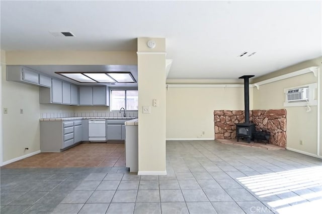 kitchen with gray cabinets, dishwasher, an AC wall unit, and a wood stove