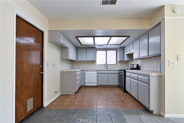 kitchen featuring dishwasher, tile counters, tile patterned floors, stainless steel stove, and gray cabinetry