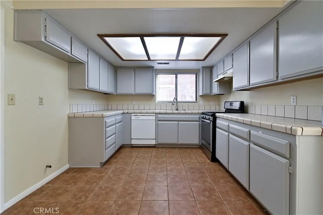 kitchen with white dishwasher, sink, light tile patterned floors, tile countertops, and stainless steel range