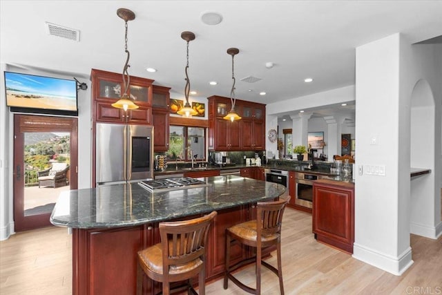 kitchen featuring decorative light fixtures, stainless steel appliances, light hardwood / wood-style floors, kitchen peninsula, and a breakfast bar