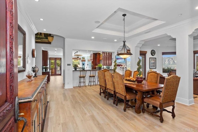 dining room featuring decorative columns, a tray ceiling, crown molding, and light wood-type flooring