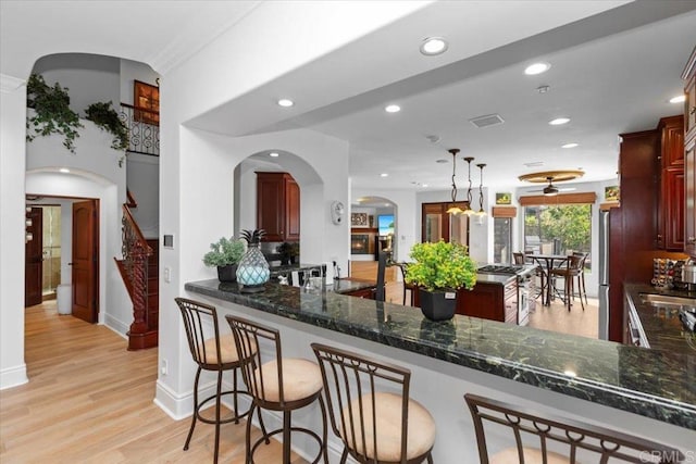 kitchen with light wood-type flooring, dark stone counters, hanging light fixtures, and kitchen peninsula