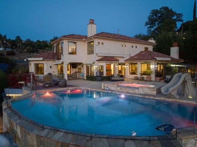 pool at dusk with an in ground hot tub, a patio, and a water slide