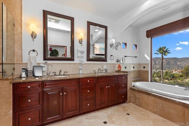 bathroom featuring a relaxing tiled tub, vanity, and a mountain view