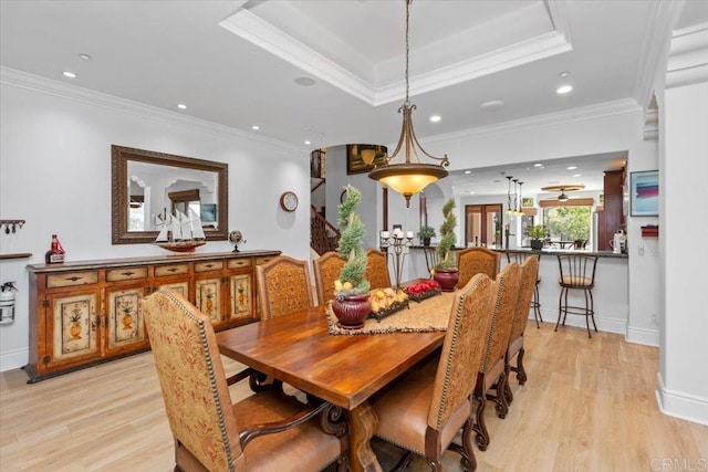 dining space with crown molding, a tray ceiling, and light wood-type flooring