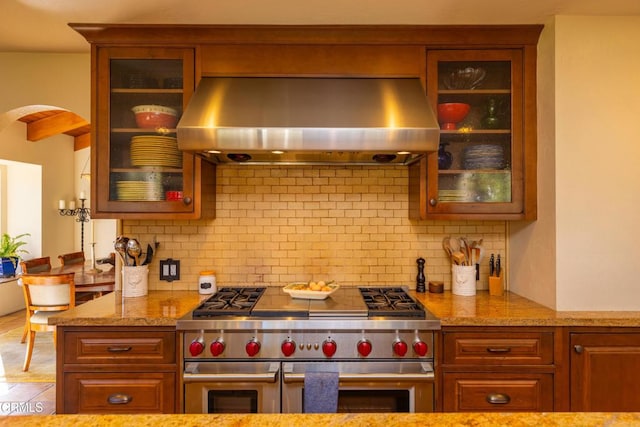 kitchen featuring light stone counters, island range hood, double oven range, and tasteful backsplash