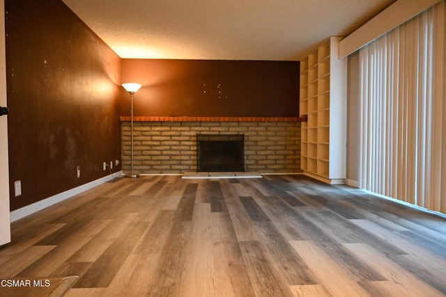 unfurnished living room featuring wood-type flooring, a brick fireplace, and built in features