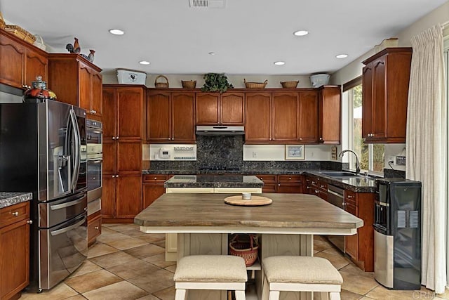 kitchen featuring sink, light tile patterned floors, appliances with stainless steel finishes, a kitchen breakfast bar, and a center island