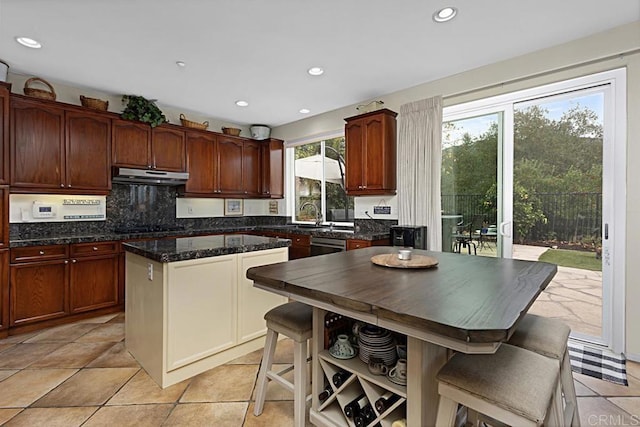 kitchen with a kitchen breakfast bar, decorative backsplash, dark stone counters, a center island, and light tile patterned floors