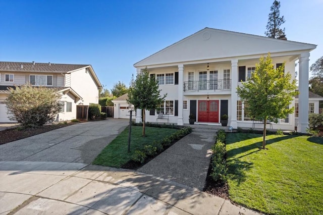 neoclassical home featuring a garage, a balcony, a front yard, and french doors