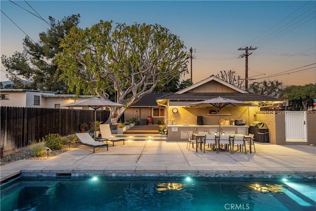 pool at dusk featuring a patio and exterior bar