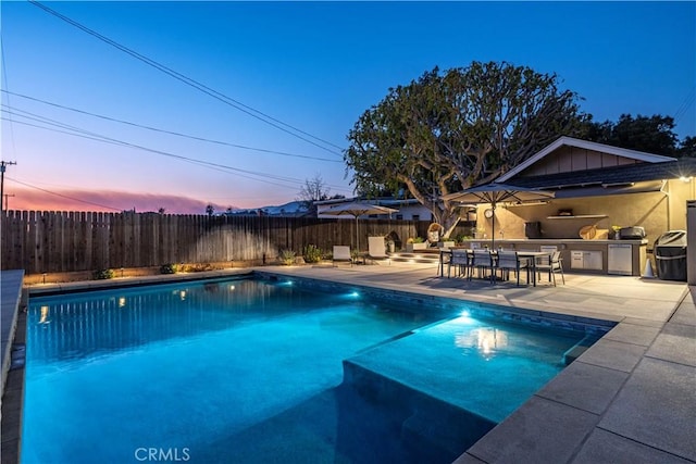 pool at dusk with a patio and area for grilling