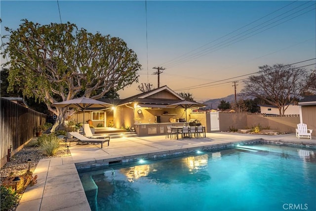 pool at dusk featuring exterior kitchen and a patio area