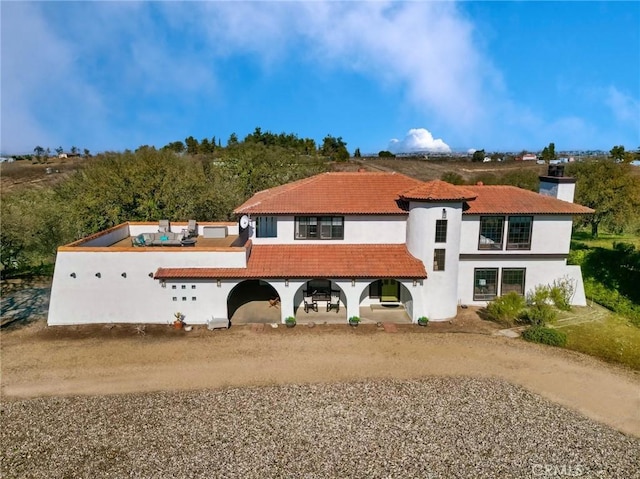 view of front facade featuring a tile roof, driveway, a chimney, and stucco siding