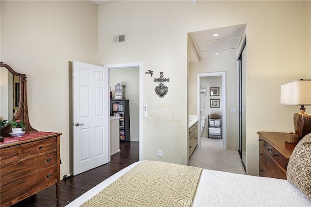 bedroom with a high ceiling, connected bathroom, and light wood-type flooring