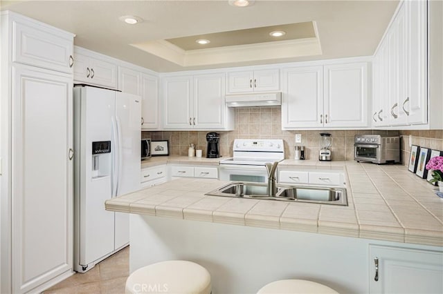 kitchen with a tray ceiling, white appliances, tile countertops, and white cabinets