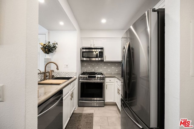 kitchen with sink, white cabinets, tasteful backsplash, light tile patterned flooring, and stainless steel appliances