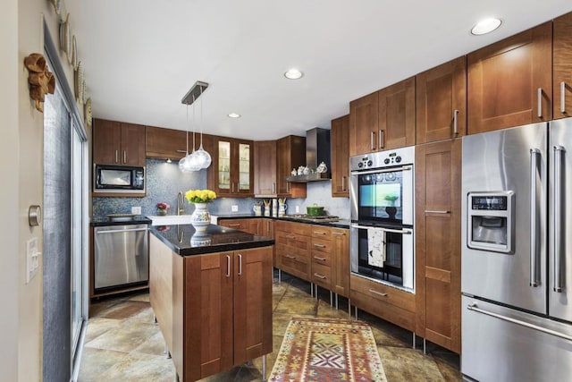 kitchen featuring pendant lighting, appliances with stainless steel finishes, tasteful backsplash, a center island, and wall chimney range hood