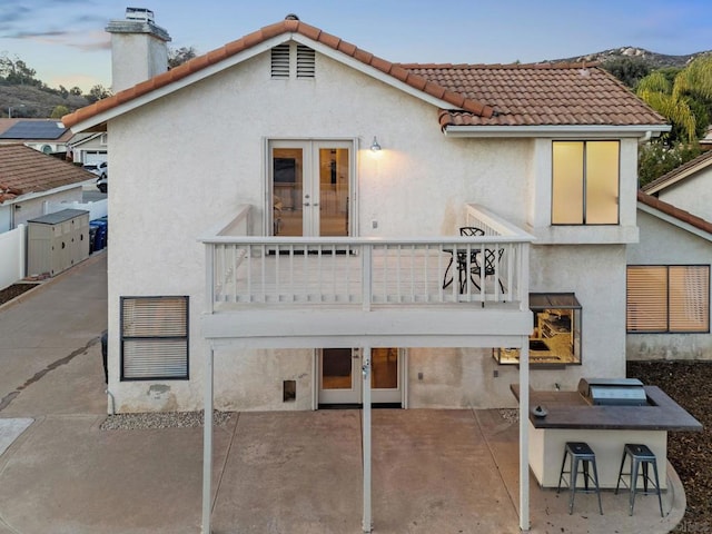 back of property featuring a balcony, exterior bar, french doors, and a patio